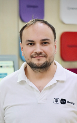 Чоловік із короткою світлою стрижкою, бородою та вусами, у білій футболці з логотипом