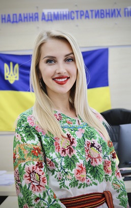 Молода жінка з довгим світлим волоссям і світлою шкірою стоїть у приміщенні.
